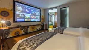 Une chambre d’hôtel dotée d’un grand téléviseur fixé au mur diffusant une vidéo, d’un lit recouvert d’une couvre-lit à motifs et d’une décoration murale sur le thème du soleil.