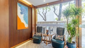 Un hall d’entrée avec un mur lambrissé en bois, deux fauteuils en cuir ornés de coussins à motifs, une petite table en bois et une plante en pot.