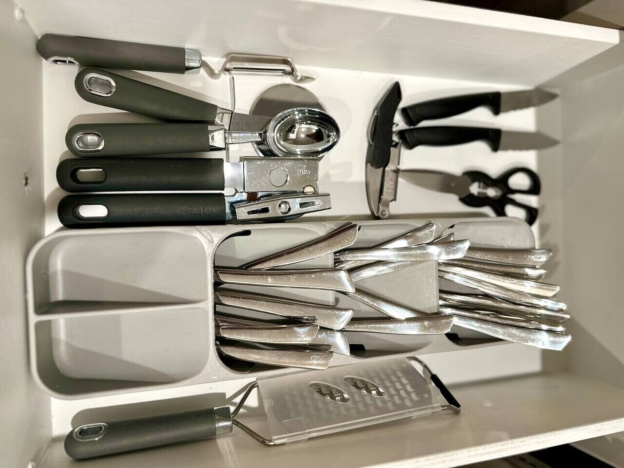 A drawer containing various kitchen utensils including spatulas, a grater, and a can opener.