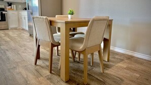 Un coin repas avec une table en bois et quatre chaises, une petite plante posée sur la table, et une cuisine en arrière-plan.