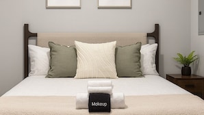 Un lit bien fait, avec une tête de lit beige, des coussins blancs et verts, et une couverture blanche. Deux œuvres d’art encadrées sont accrochées au mur au-dessus du lit.