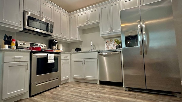 Une cuisine moderne avec des meubles blancs, des appareils en acier inoxydable et un plancher en bois.