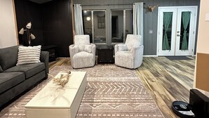 A modern living room with a dark wood ceiling, a grey sofa, a white coffee table, and two white armchairs. - Charming 2-bedroom cottage waterfront on the little Deschutes River  La Pine, OR (La Pine)