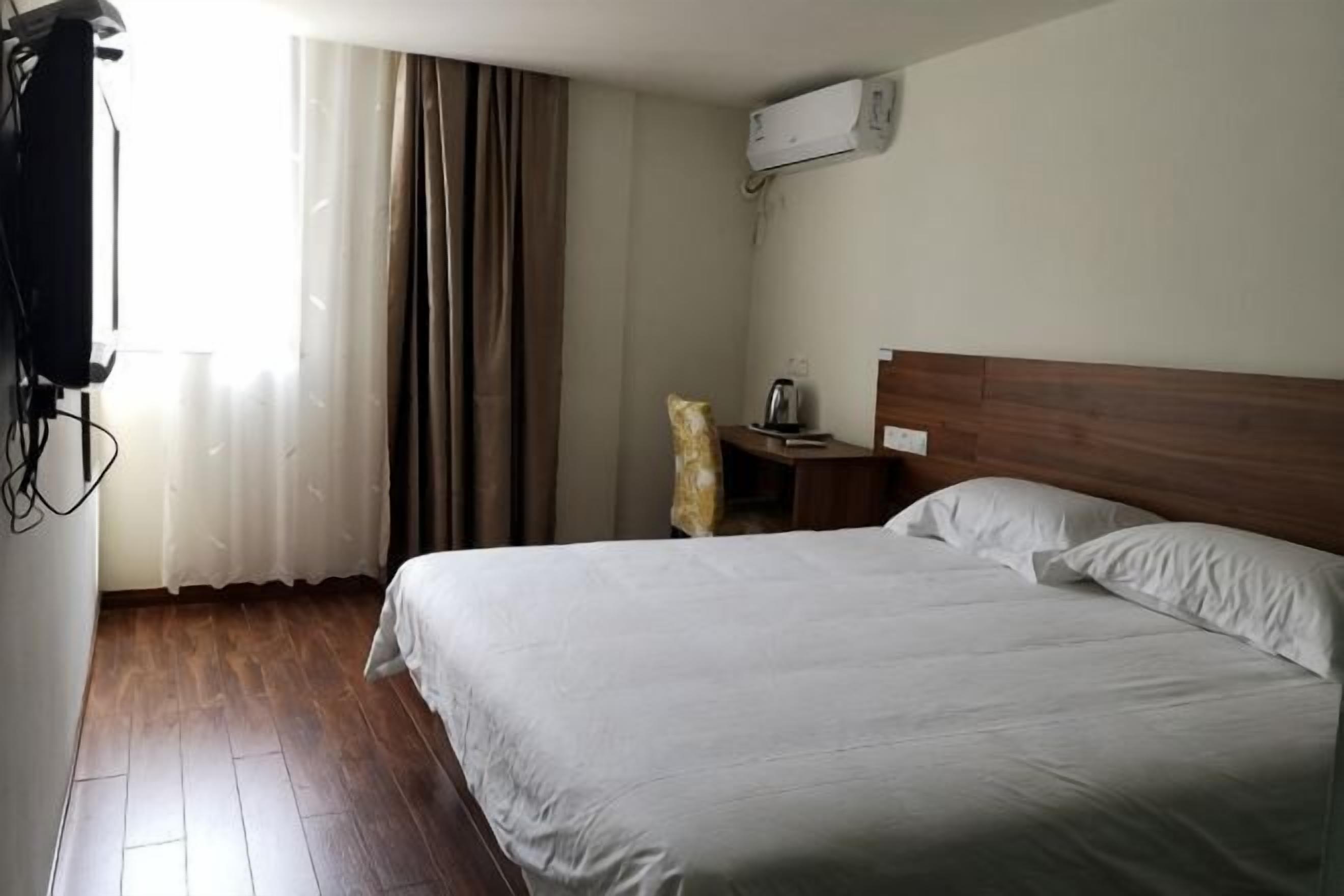 Une chambre d’hôtel avec un plancher en bois, un lit avec du linge de maison blanc, une table de chevet avec une lampe et une fenêtre avec des rideaux.