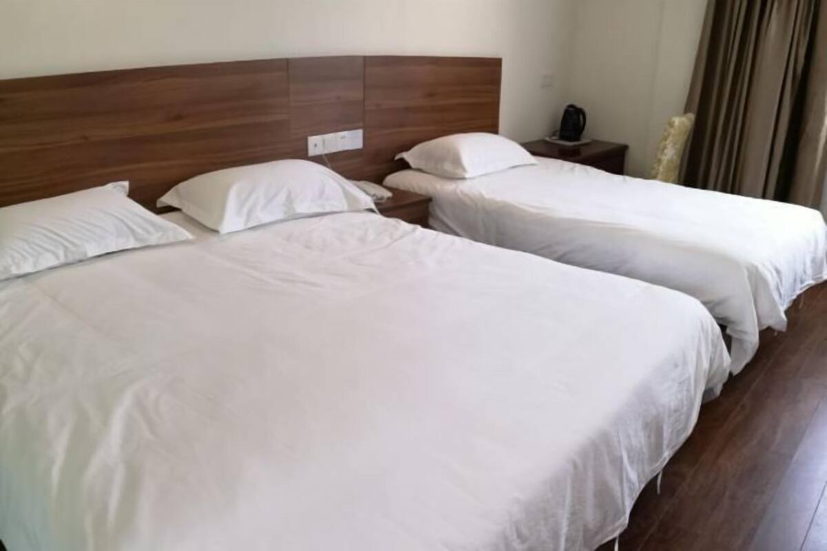 A hotel room with two beds, wooden headboard, white bedding, bedside tables, and a nightstand with a phone and a kettle.