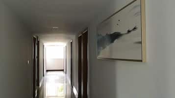 Un pasillo con una obra enmarcada en la pared, una puerta al final y una fuente de luz brillante al fondo.