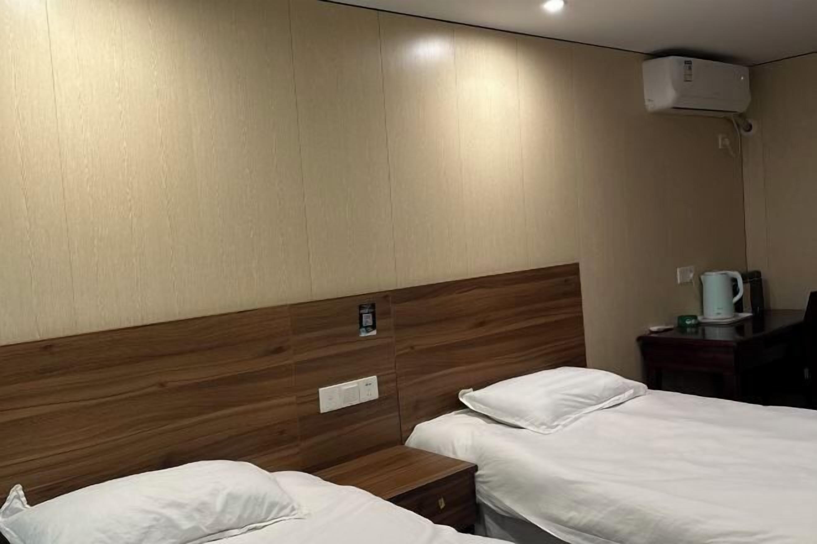 Quarto de hotel com duas camas, cabeceira de madeira, mesas de cabeceira, cafeteira e ar condicionado.