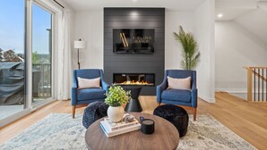 A modern living room with two blue armchairs, a fireplace, a mounted sign, and a large window.