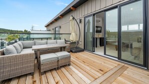 A modern outdoor patio with wicker furniture, a glass door leading to a room, and a view of the landscape.