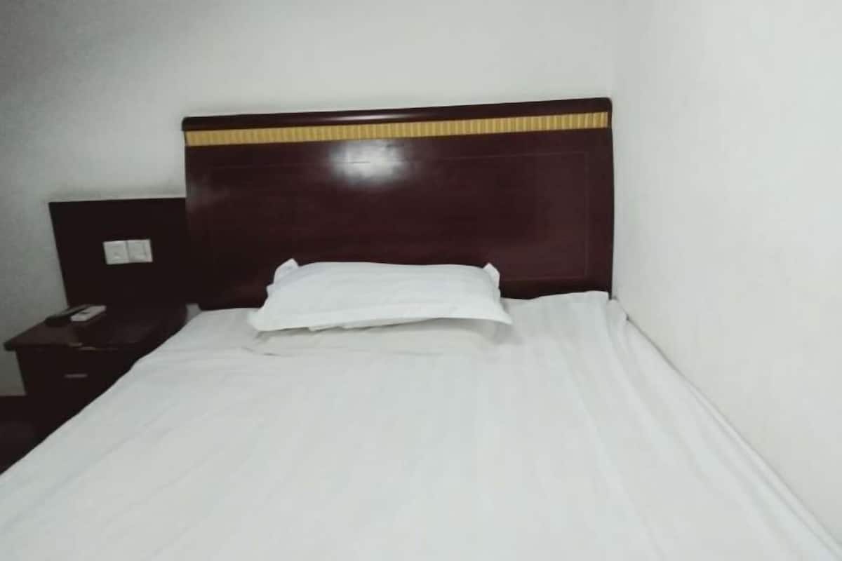 Una cama individual con cabecera de madera, almohada blanca y pared lisa.