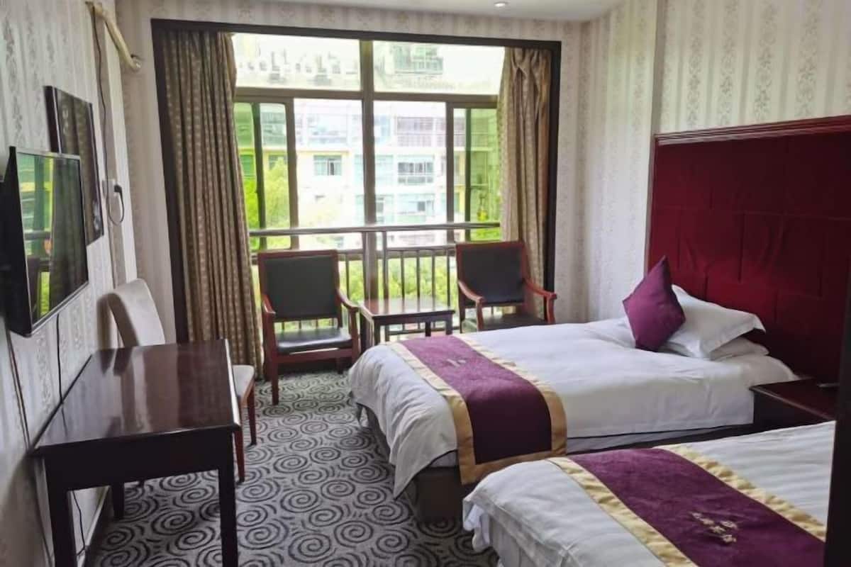 Una habitación de hotel con dos camas, un escritorio, televisión y balcón con sillas.