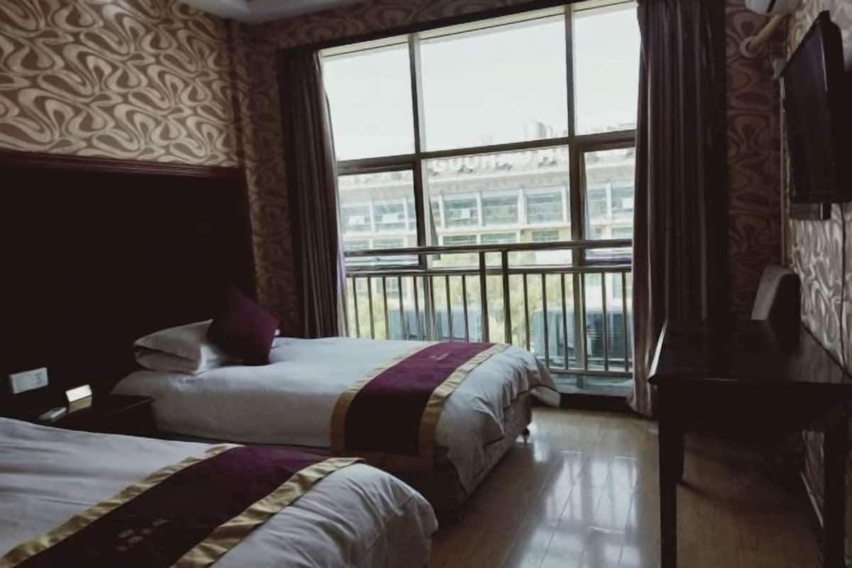 Habitación de hotel con dos camas, un ventanal con vistas a edificios y un escritorio de madera.