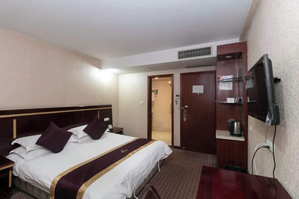 Habitación de hotel con cama, televisión, escritorio y puerta que da a un baño.