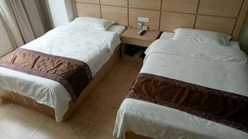 A hotel room with two single beds, a wooden headboard, a bedside table with a lamp, and a nightstand.