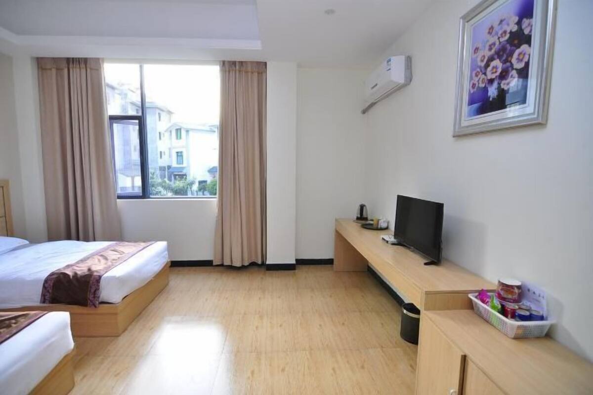 A hotel room with a bed, a TV, a desk, a window with curtains, and a picture on the wall.