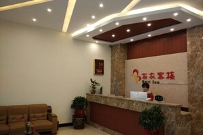 A hotel reception area with a receptionist desk, a digital clock, and a sofa.