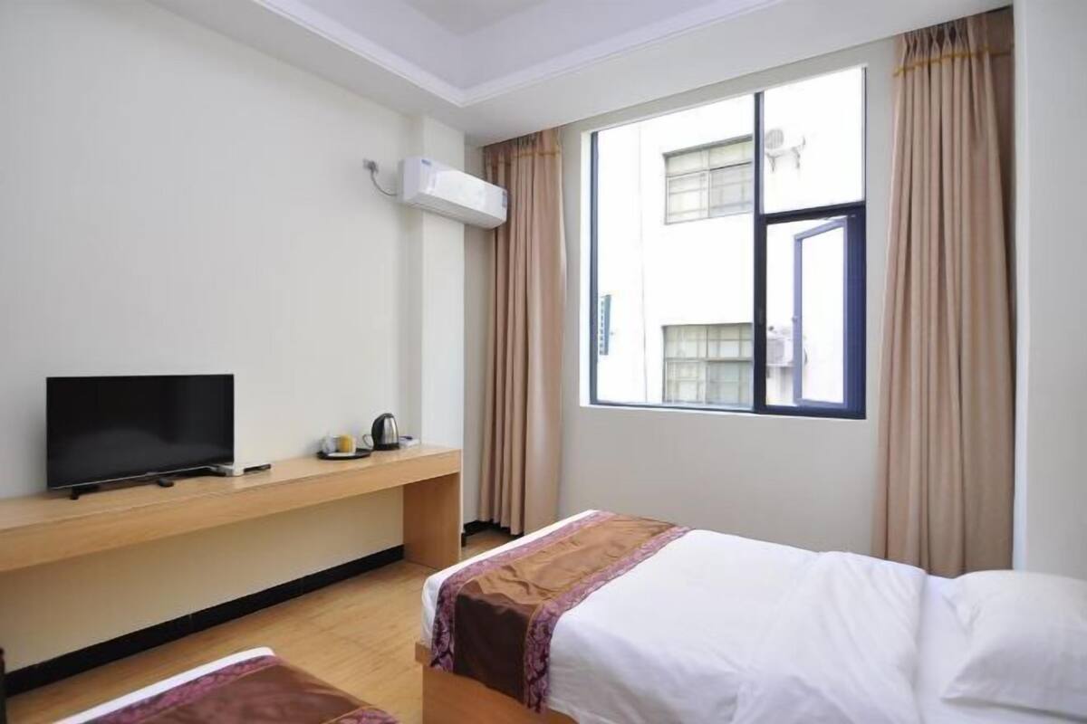 A hotel room with a bed, a TV, a desk, and a window with curtains.