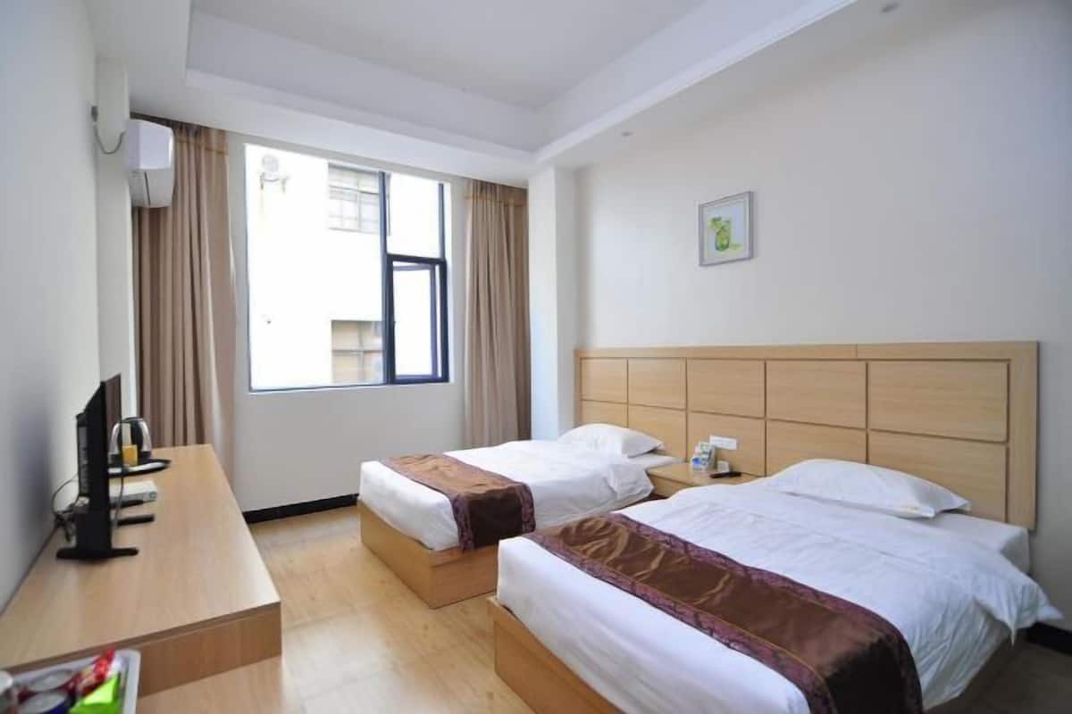 A hotel room with two beds, a desk, a TV, and a window with curtains.