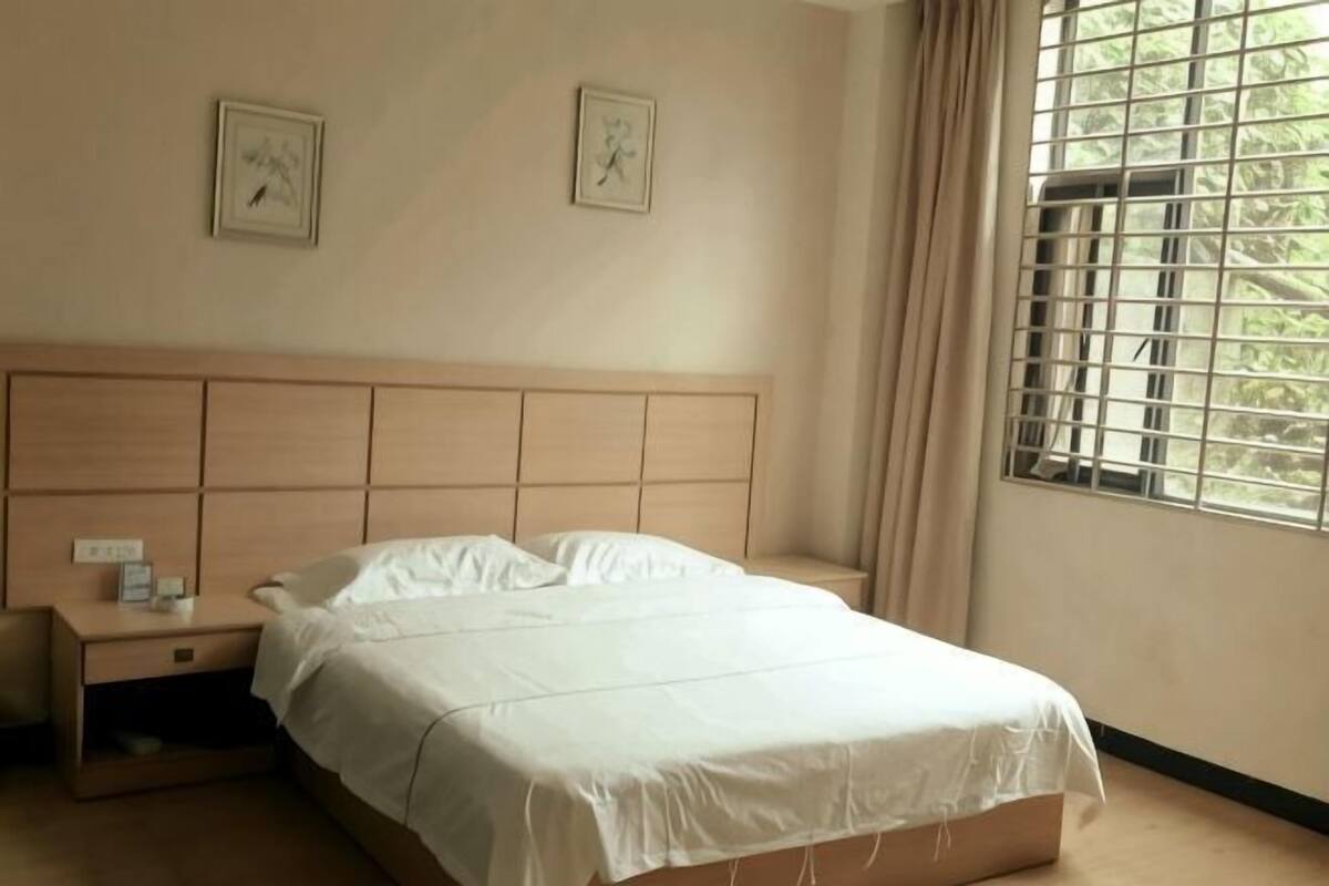 A bedroom with a bed, nightstand, and window with curtains.