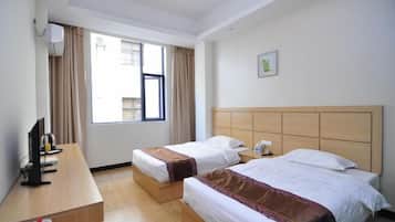 A hotel room with two beds, a desk, a TV, and a window with curtains.
