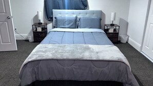 A neatly arranged bedroom with a bed, two bedside tables, a nightstand, a window with curtains, and a door. - Convenient Walkout Basement Apartment, private entrance in Aurora with WiFi (Aurora)