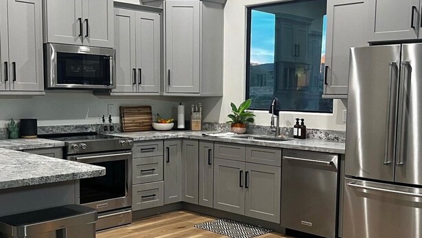 Une cuisine moderne avec des meubles gris, des appareils en acier inoxydable, un plancher en bois et une fenêtre offrant une vue.