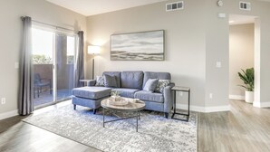 A modern living room with a grey sofa, a coffee table, and a large window with curtains. - Sunny San Diego Condo w/ Pool Access Near Wineries (San Diego)