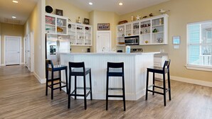 A kitchen with a central island, white cabinetry, and a view of the living area. - Pet Friendly, Golf Cart Included, Walk to the Beach (Port Aransas)