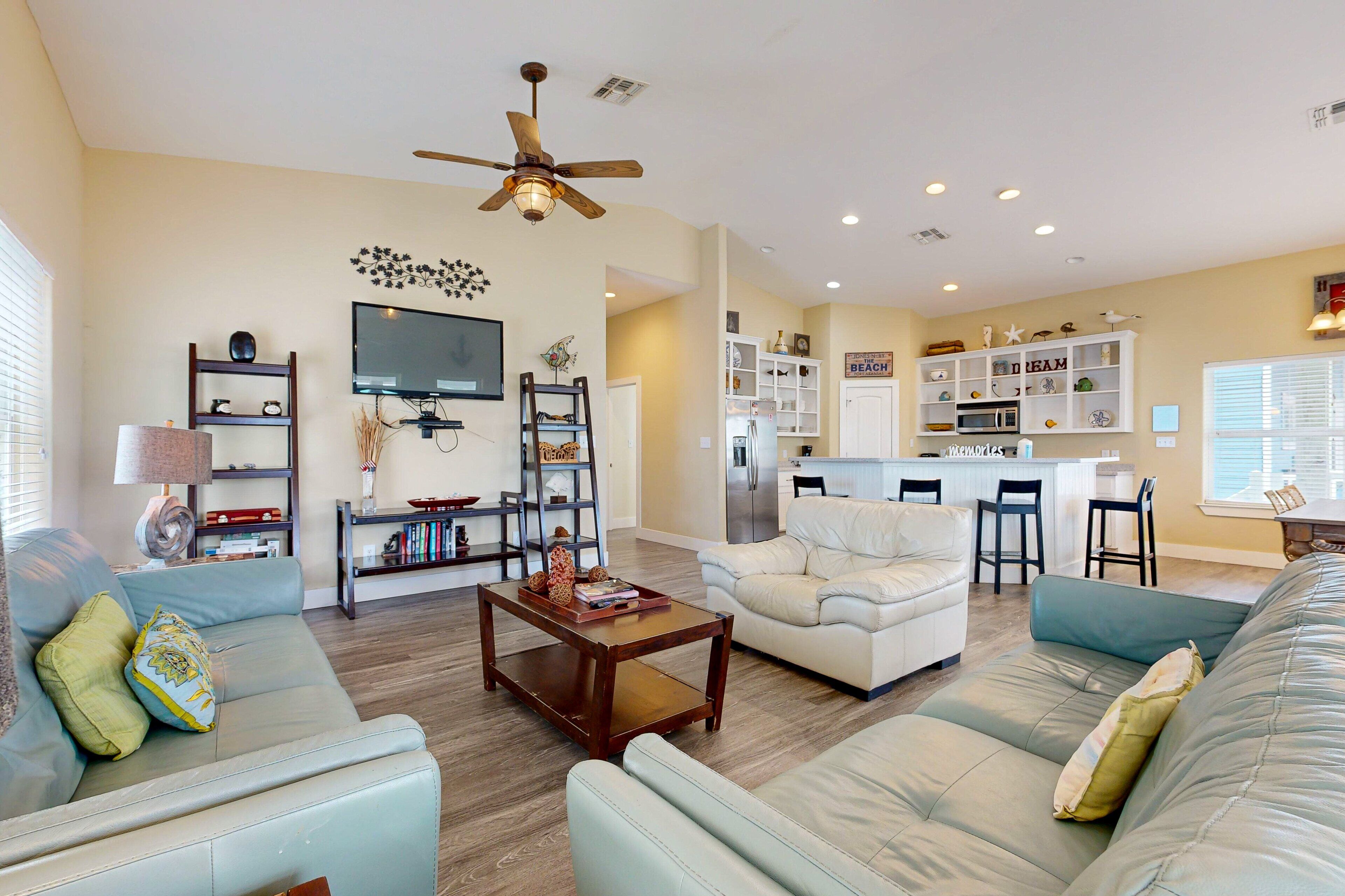A spacious living room with a sofa, coffee table, and a TV. There is a kitchen area with a refrigerator and a dining table.