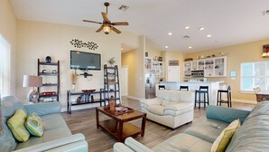 A spacious living room with a sofa, coffee table, and a TV. There is a kitchen area with a refrigerator and a dining table. - Pet Friendly, Golf Cart Included, Walk to the Beach (Port Aransas)