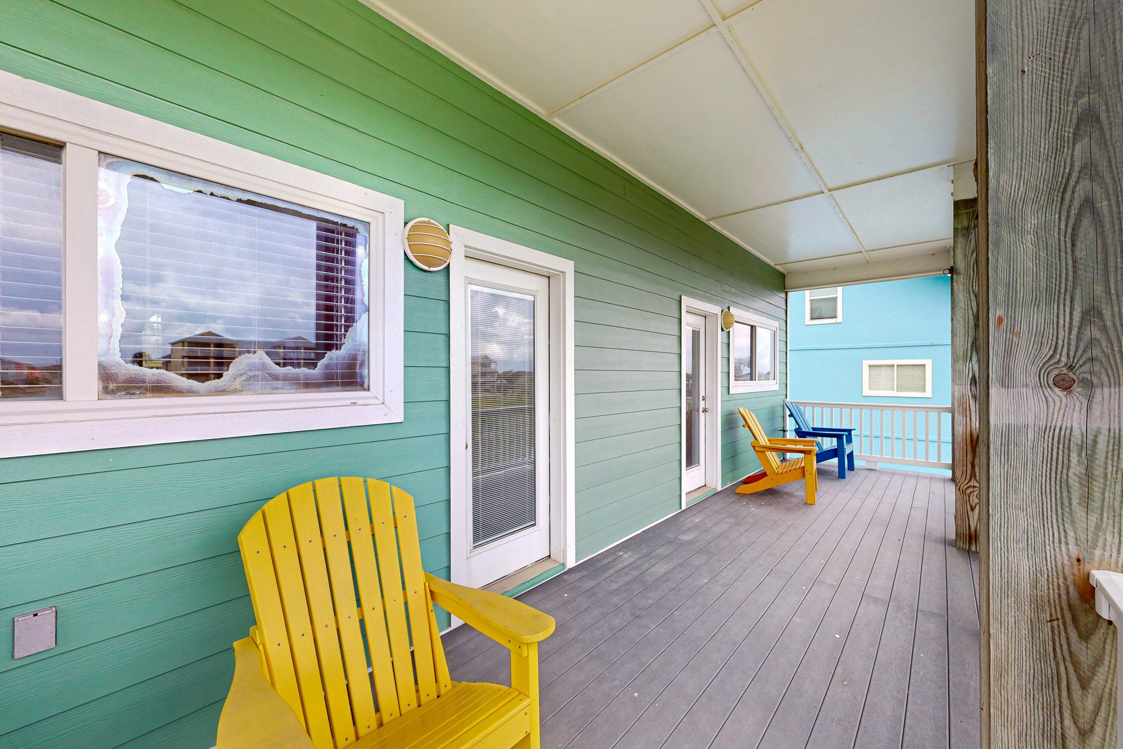 A wooden deck with a green building, a yellow chair, and a blue chair.