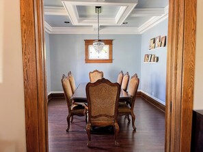 A dining room with a wooden table and chairs, a chandelier, and framed pictures on the wall.