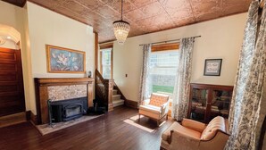 A spacious living room with hardwood floors, a fireplace, a staircase, and a large window with curtains.