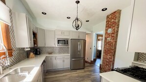A modern kitchen with white cabinets, stainless steel appliances, and a herringbone wood floor.