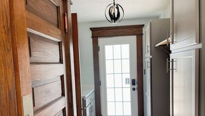 A hallway with wooden doors, a white door with a window, and a bench.