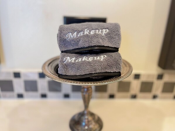 Una pila de toallas grises con la palabra 'Makeup' bordada, sobre un elegante expositor de vidrio.
