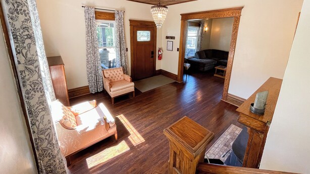 A spacious living room with a wooden floor, a plush armchair, a sofa, and a chandelier.