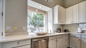 Una cocina moderna con armarios blancos, lavavajillas de acero inoxidable y un ventanal que proporciona luz natural.