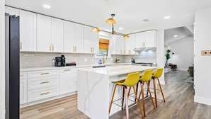 Una cocina moderna con gabinetes blancos, una isla de mármol y taburetes amarillos.