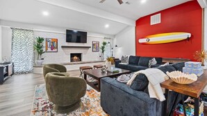 Una sala de estar moderna con chimenea, ventilador de techo y una tabla de surf en la pared.