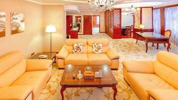 A hotel room with a sofa set, a coffee table, a dining table, and a chandelier.