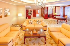 A hotel room with a sofa set, a coffee table, a dining table, and a chandelier.