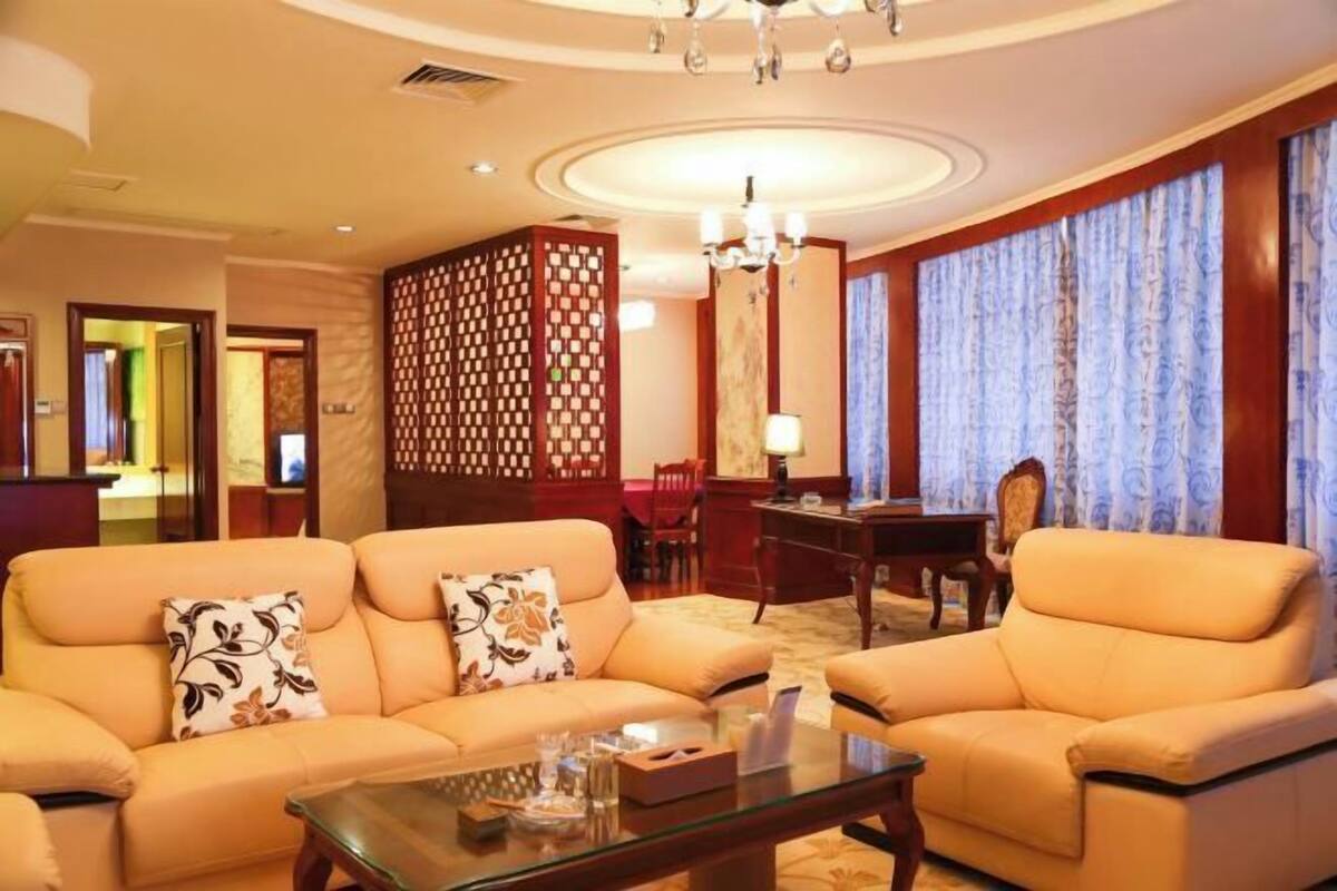 A hotel room with a sofa set, a glass coffee table, a desk, and a chair.