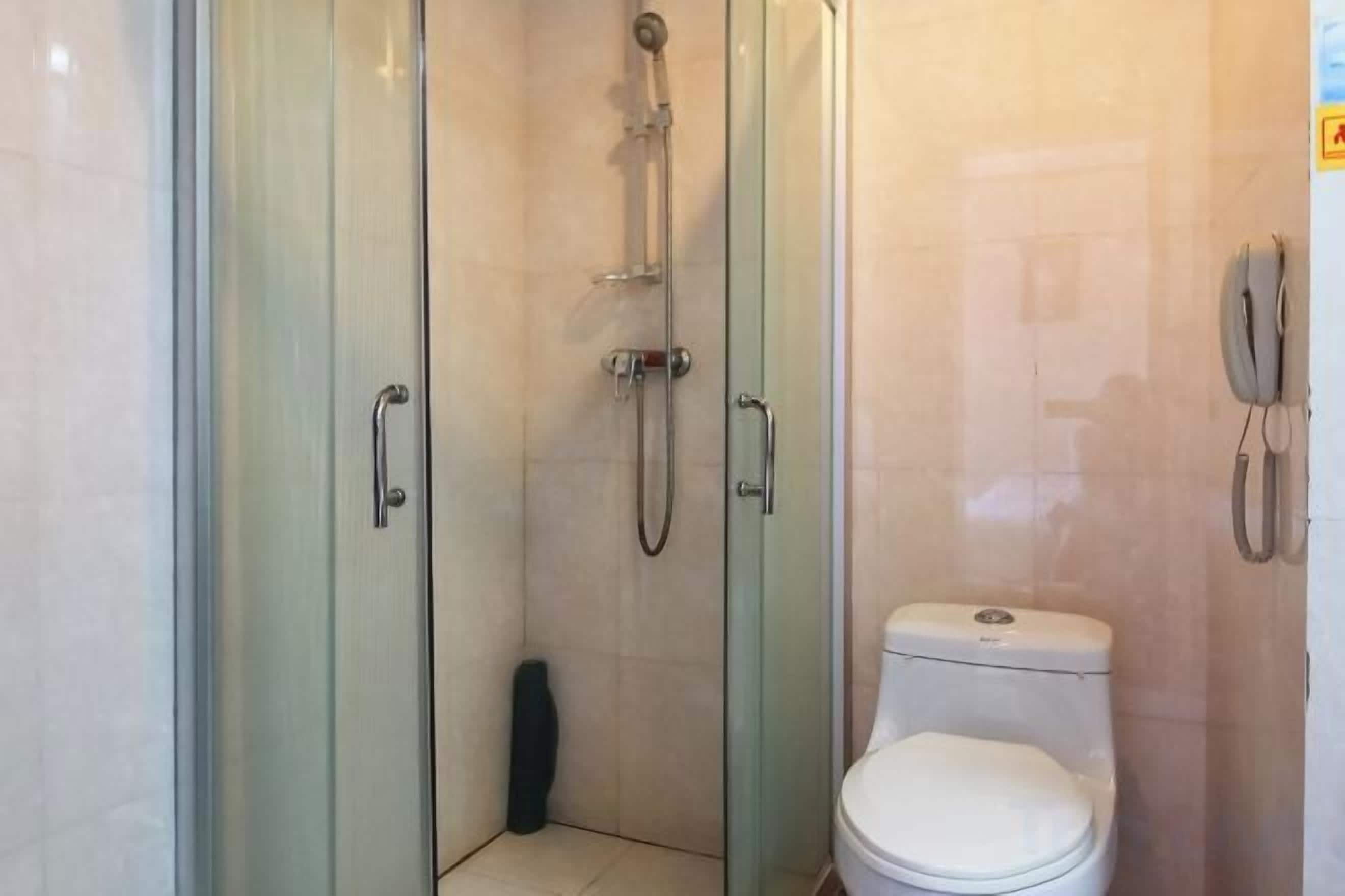 Une cabine de douche fermée par des parois en verre, dotée d’un pommeau de douche à main, de toilettes et d’un téléphone fixé au mur.