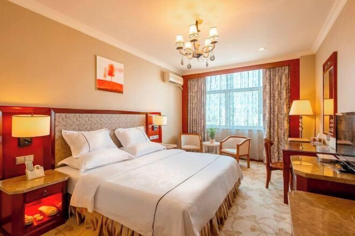A hotel room with a large bed, a desk, a chair, a TV, and a window with curtains.