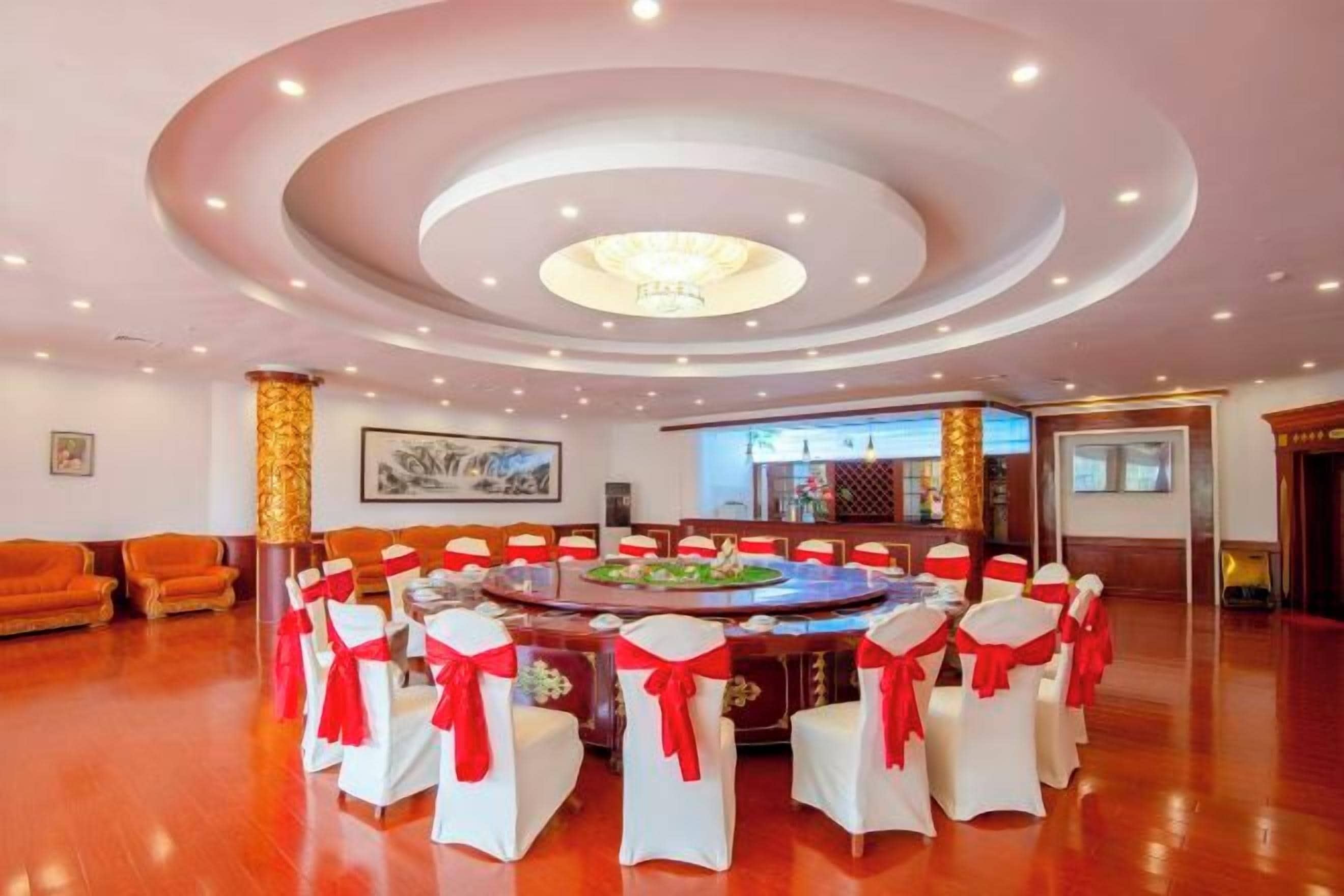 A spacious hall with a central round table surrounded by chairs, a bar area, and a seating area with sofas.