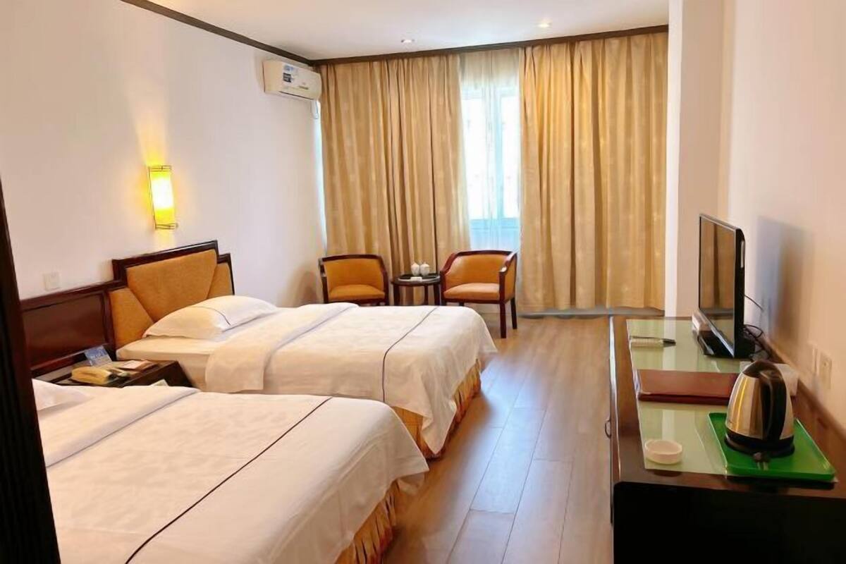 A hotel room with two beds, a desk with a television, a chair, and a window with curtains.
