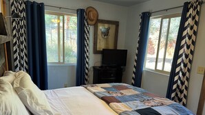 Ein Schlafzimmer mit Bett, Vorhängen, einem Fernseher und einem an der Wand hängenden Bilderrahmen.
