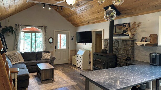 Ein gemütliches Wohnzimmer mit Kamin, Holzbalkendecke und Steinwand. Es gibt ein Sofa, einen Couchtisch und einen an der Wand befestigten Fernseher.