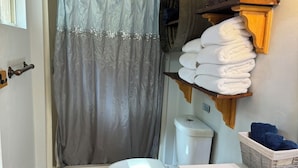 Ein Badezimmer mit Duschvorhang, Toilette, Waschbecken und Ablagefläche für Handtücher.